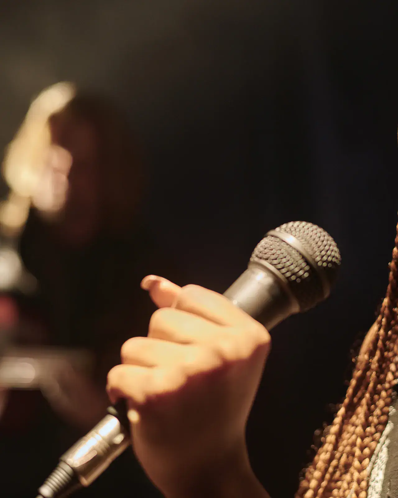 Vocalist singing with braided hair in dramatic lighting — Concerto Music Place choir-competition adjudication