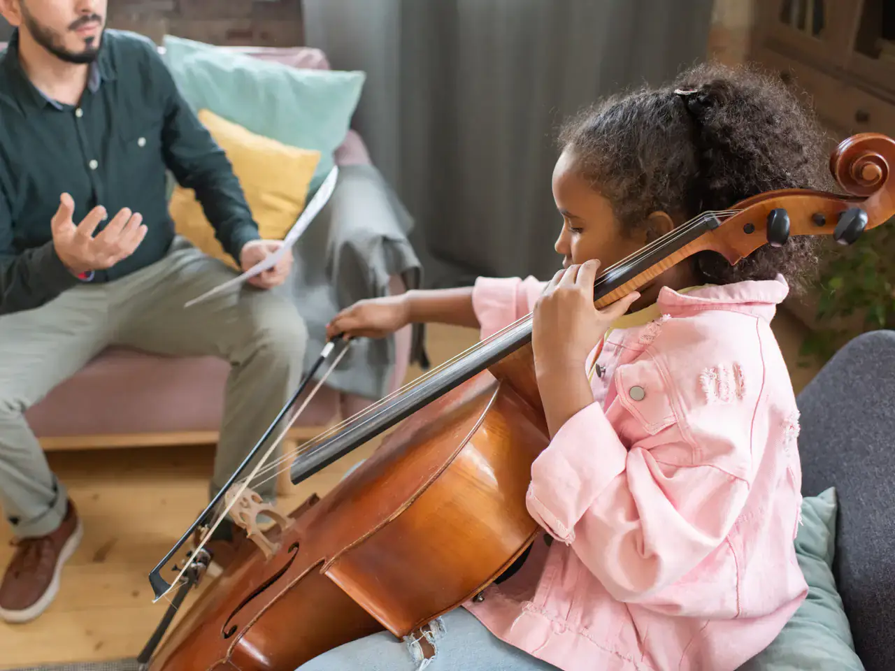 A trainer coaching a young student one-on-one through a cello lesson at home — personalized training with Concerto Music Place
